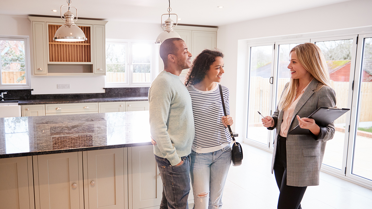 Female Realtor Showing Couple Interested In Buying Around House